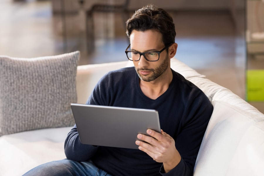 A man is looking into the tablet screen and lightly smiling